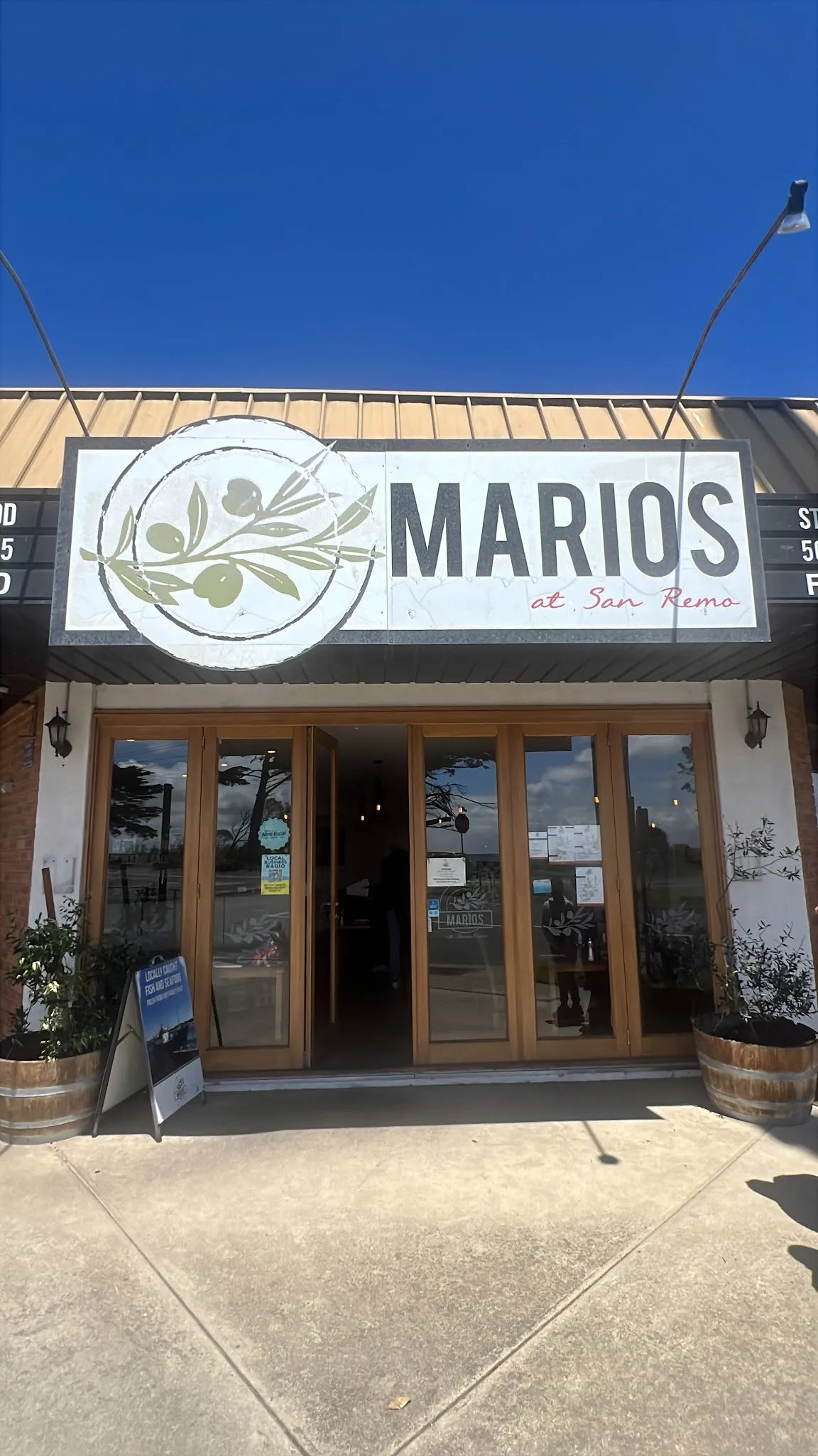 Mario's at San Remo restaurant exterior with large signage, timber doors and barrel planters under blue sky