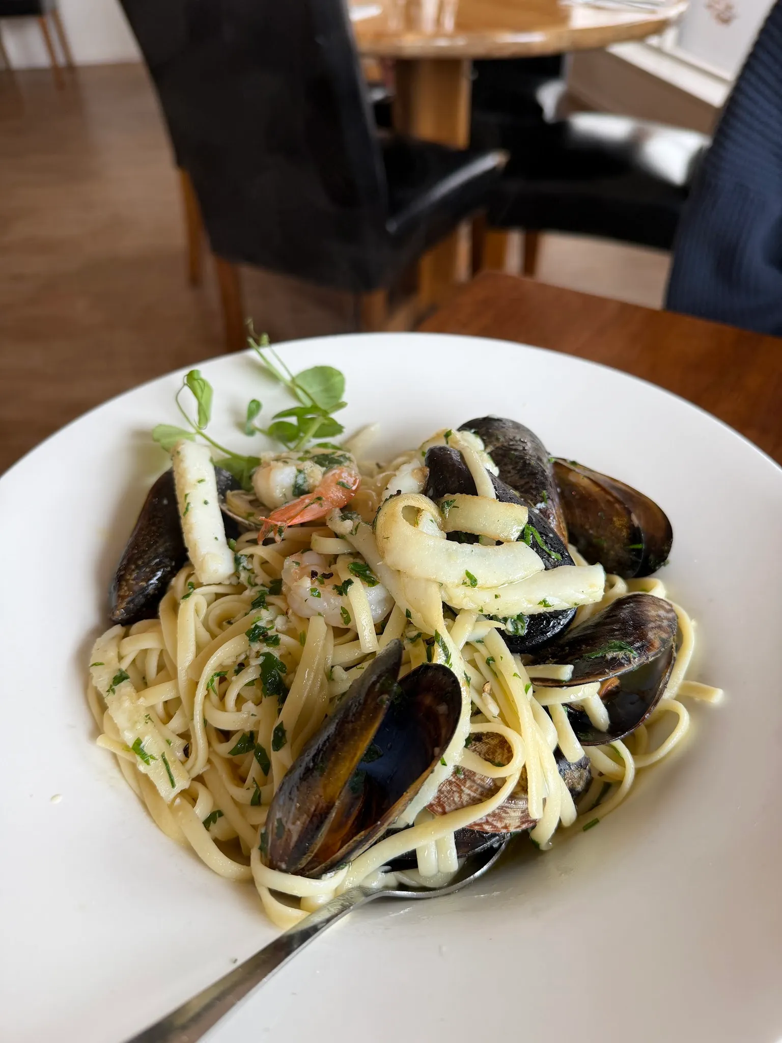 Seafood linguine with mussels, prawns and calamari in white bowl with restaurant interior in background