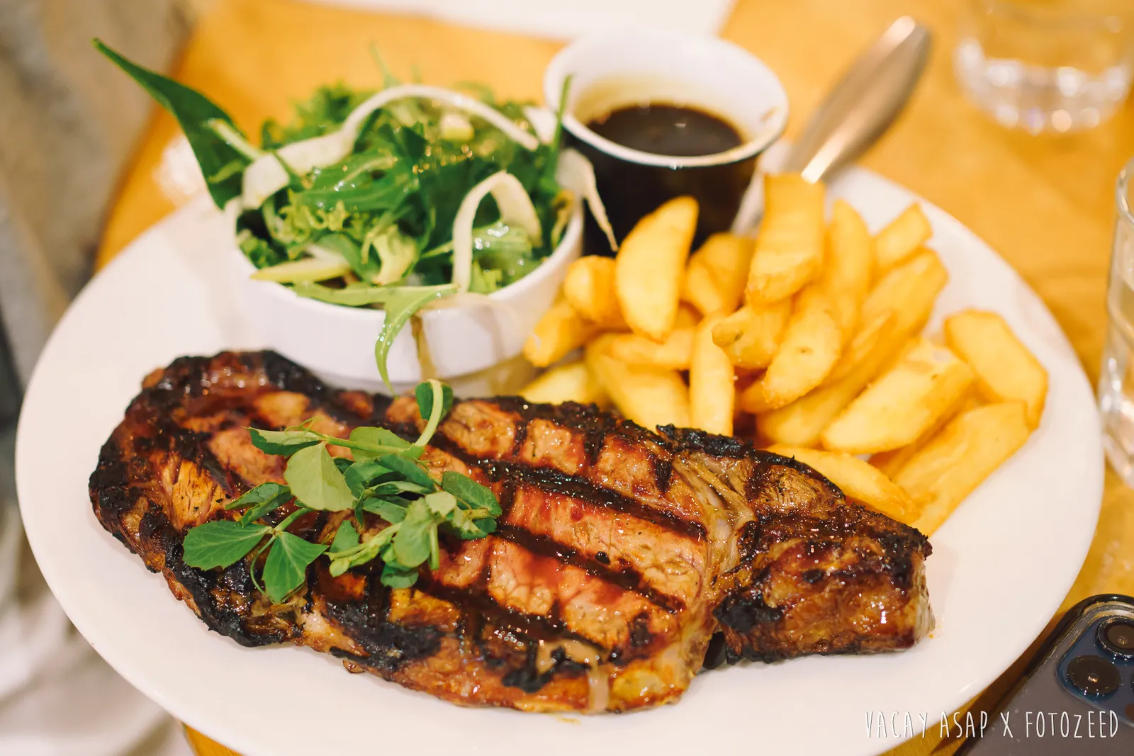 Char-grilled scotch fillet steak with chips, salad and jus on white plate