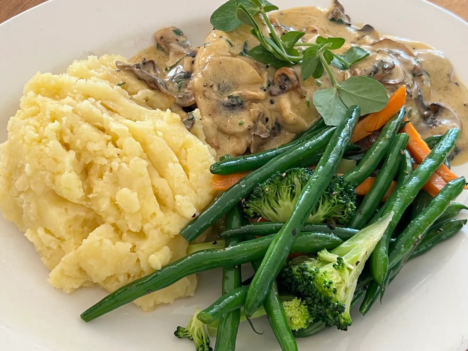 Chicken in mushroom cream sauce with mash and seasonal vegetables on white plate