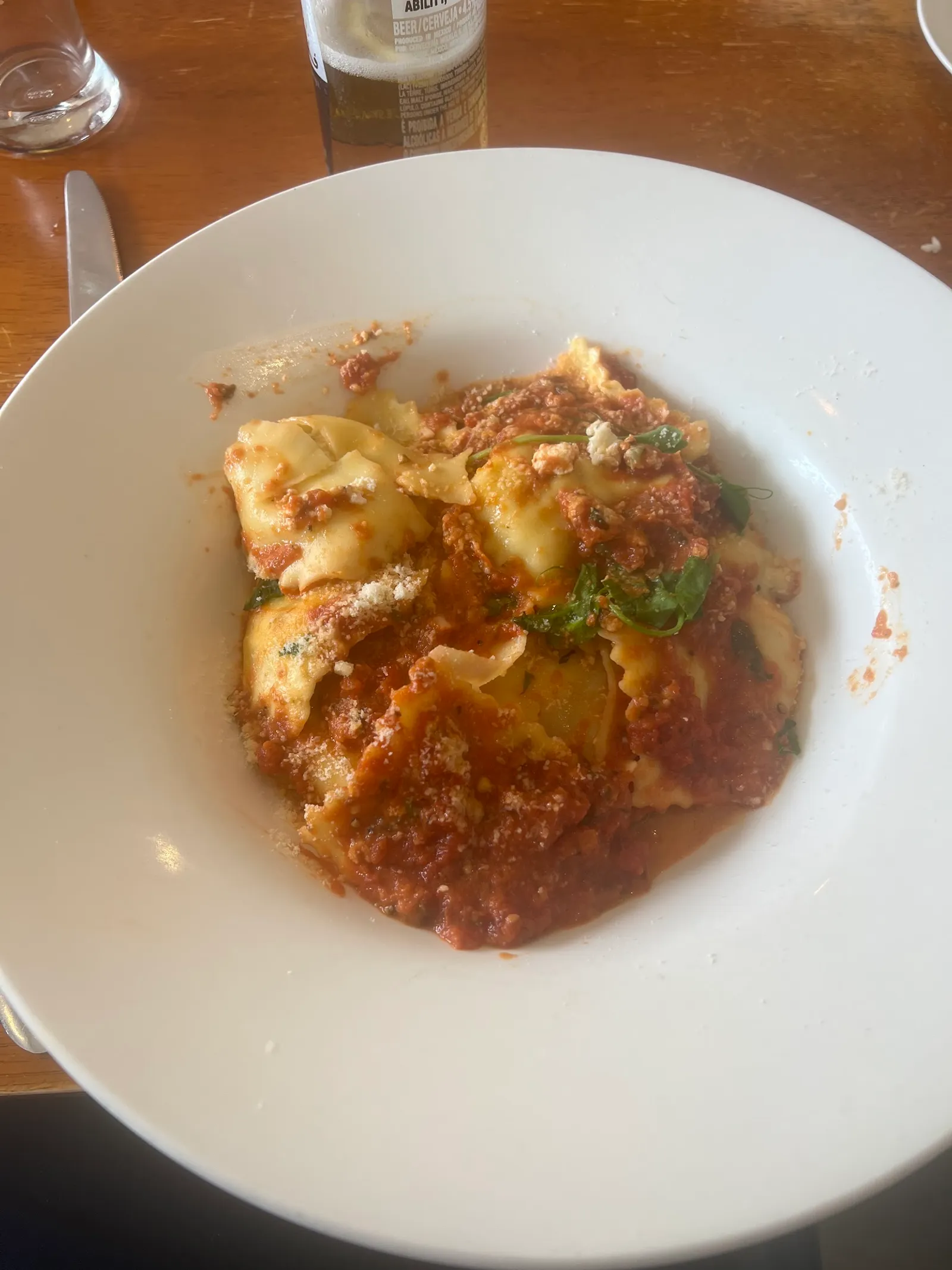House-made ravioli in meat bolognese sauce with basil and cheese in white bowl