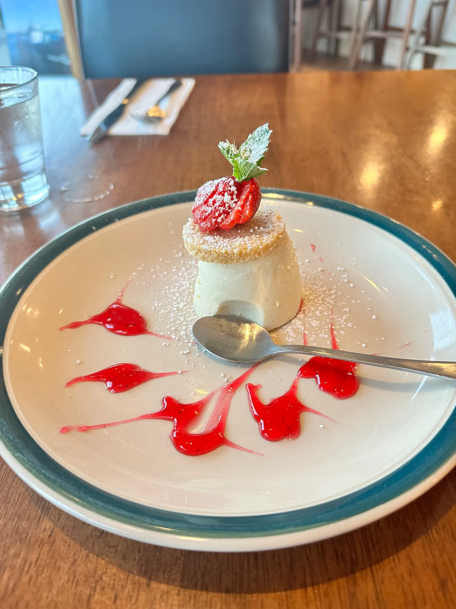 Panna cotta with strawberry and mint on teal-rimmed plate with red berry coulis decoration