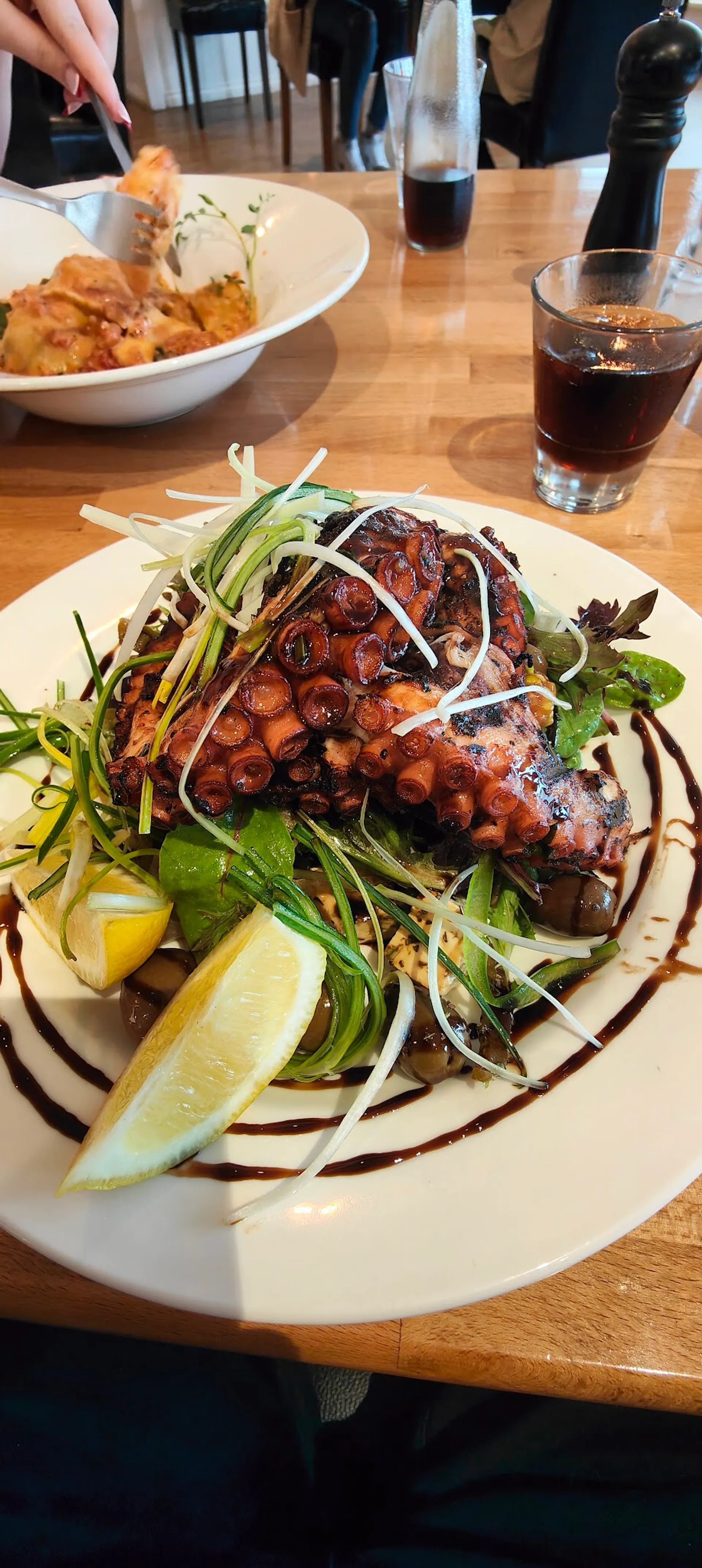 Char-grilled octopus on pea shoot and fennel salad with balsamic and lemon on white plate