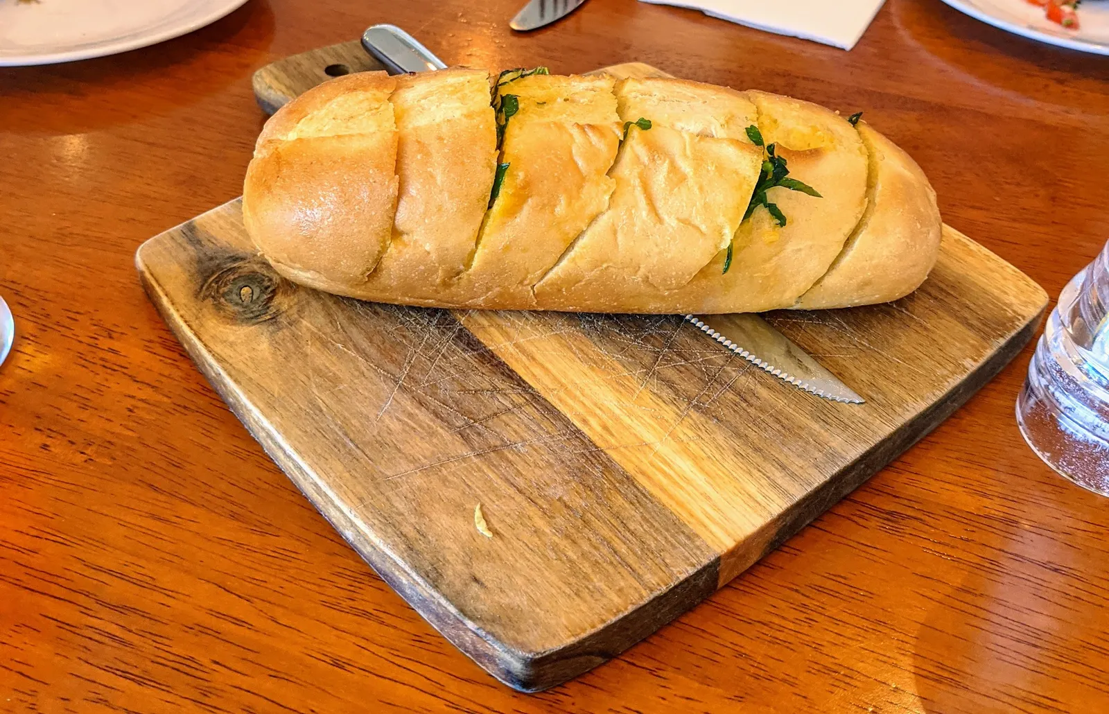 Garlic herb bread loaf on dark timber board with bread knife, golden baked with parsley butter