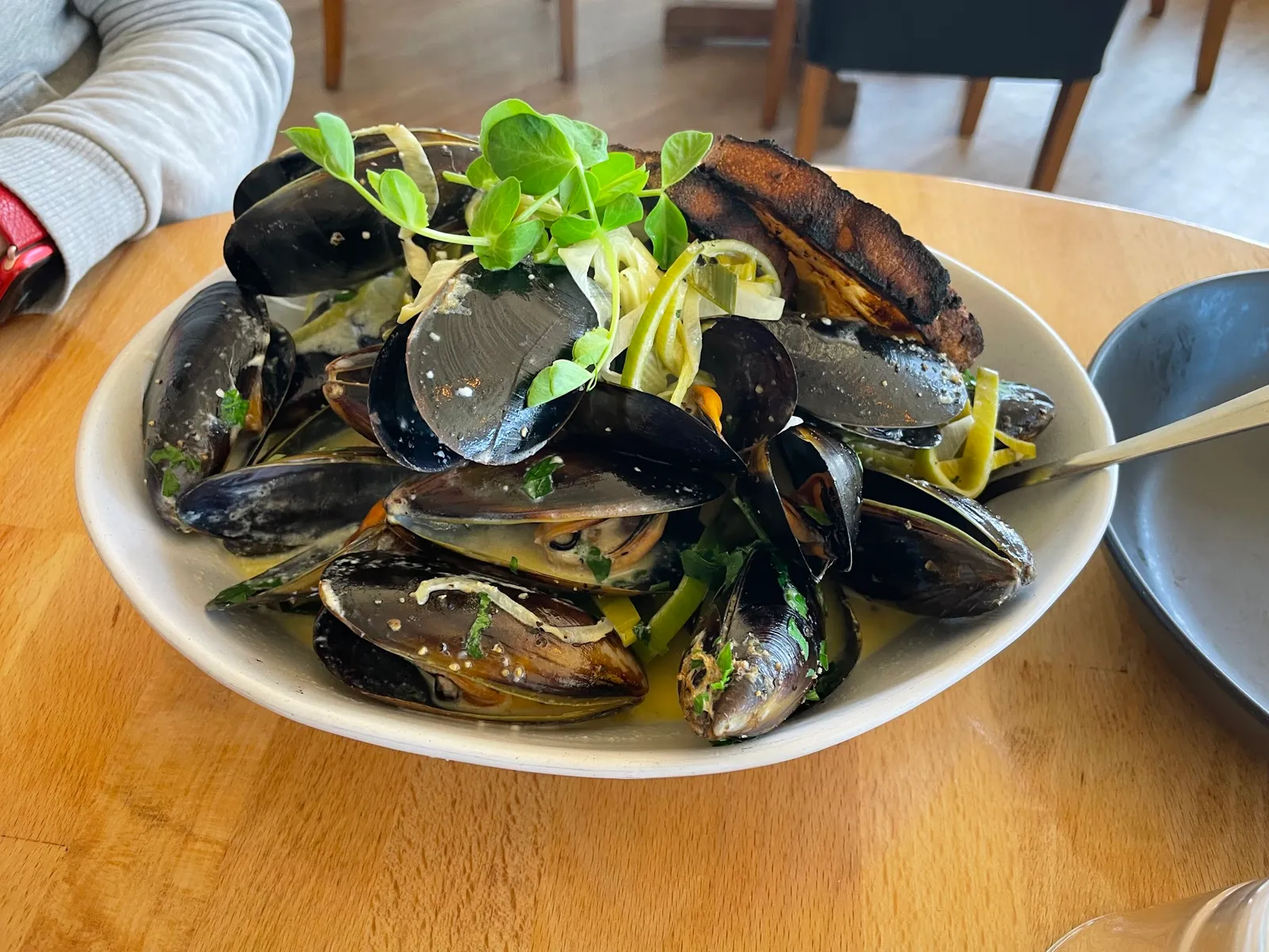 Steamed black mussels with fettuccine in white wine herb broth, pea shoots in white bowl